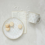 White ceramic mug and plate with decorative patterns on a light gray surface