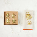 Gold gingerbread man and angel decorations in packaging on a textured white surface