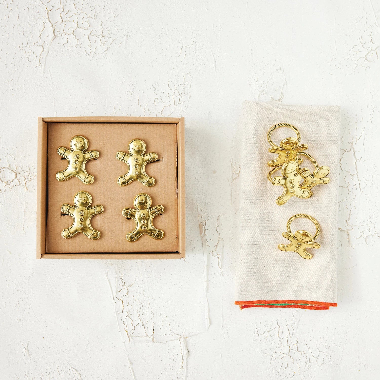 Gold gingerbread man and angel decorations in packaging on a textured white surface