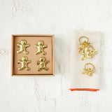 Gold gingerbread man and angel decorations in packaging on a textured white surface